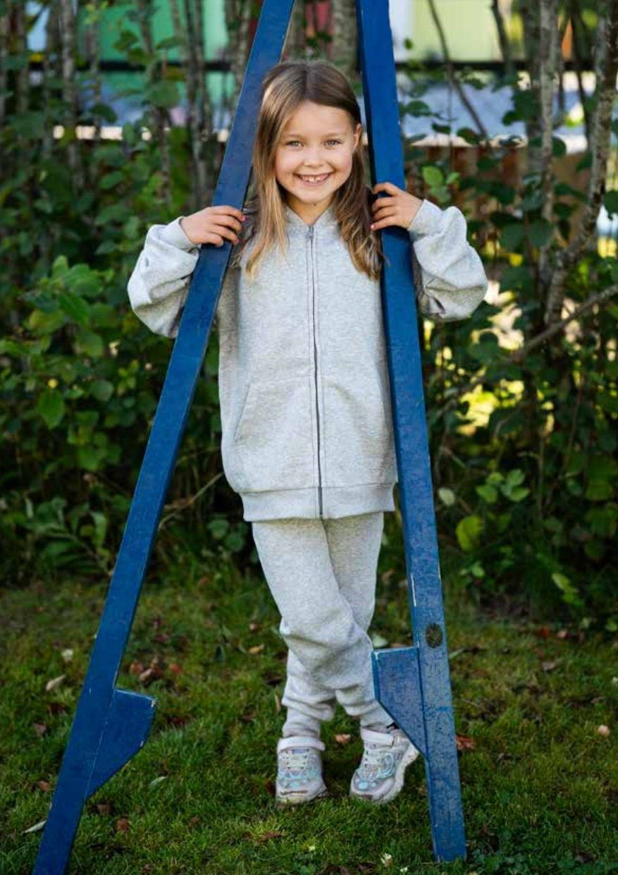 Jente i grå dress som står mellom et par store blå stylter på plenen.